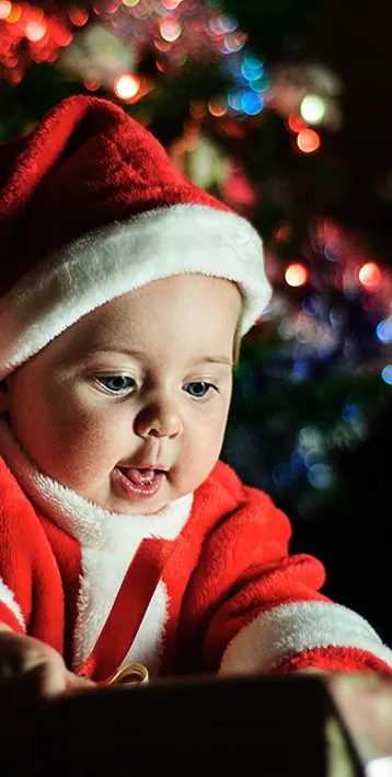 baby in santa outfit in front of christmas tree