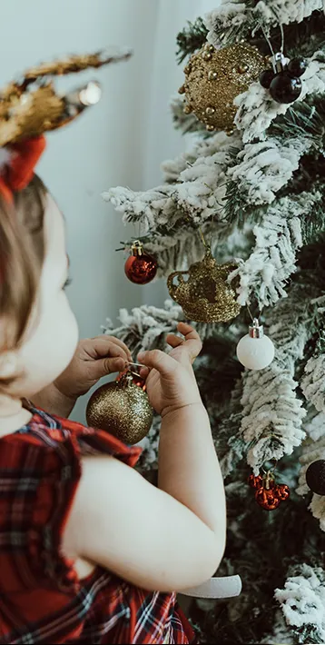 toddler in red plaid decorating flocked christmas tree